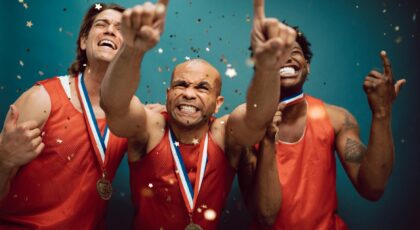 Three athletes celebrating victory with medals and confetti against a blue background.