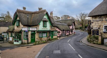 Picturesque street in an English village with traditional thatched roof buildings and shops.