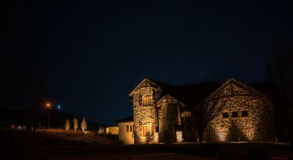 A beautifully lit stone mansion stands under a star-filled night sky, exuding a serene and mystical charm.