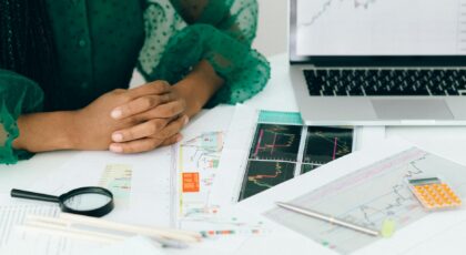 A person analyzes financial charts and graphs at a desk, indicating business trading activity.