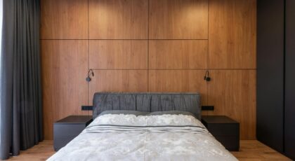 Comfortable bed with pillows and blanket placed in cozy bedroom with wooden walls and minimalist furniture