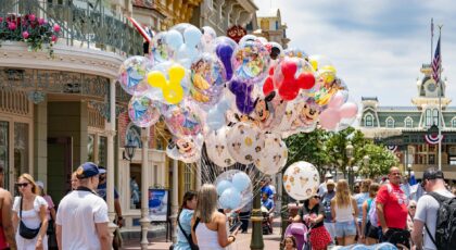 Colorful Disney-themed balloons on Main Street, USA at Disney World, with a lively crowd enjoying a sunny day.