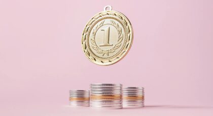 A gold medal and stacks of coins on a light pink backdrop, symbolizing victory and wealth.