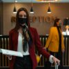 A woman in a mask stands at a hotel reception desk holding paper, welcoming service