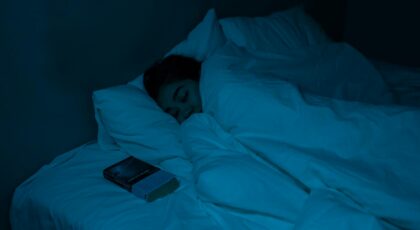 A woman peacefully sleeping with a book under blue night lighting, showcasing a cozy bedtime atmosphere.