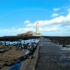 Scenic view of St Mary's Lighthouse on a clear day with a rainbow and blue sky.