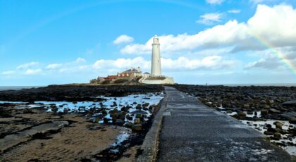 Scenic view of St Mary's Lighthouse on a clear day with a rainbow and blue sky.