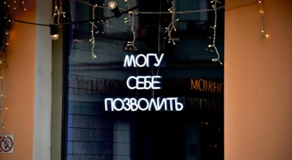 Neon sign in Russian with decorative string lights at night.