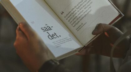 Person holding and reading an open book with visible text.