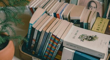 A collection of books neatly arranged in a suitcase next to a potted plant on a wooden table, creating a cozy indoor setting.