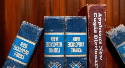 Close-up of old encyclopedias and a dictionary on a wooden shelf, showcasing vintage charm.