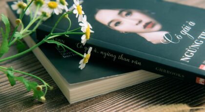 Close-up of a book with chamomile flowers on a wooden surface, conveying a peaceful reading atmosphere.